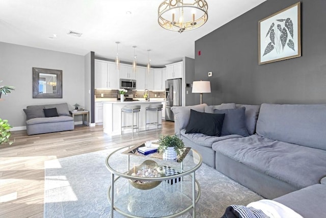 living room featuring light wood finished floors, a chandelier, and baseboards