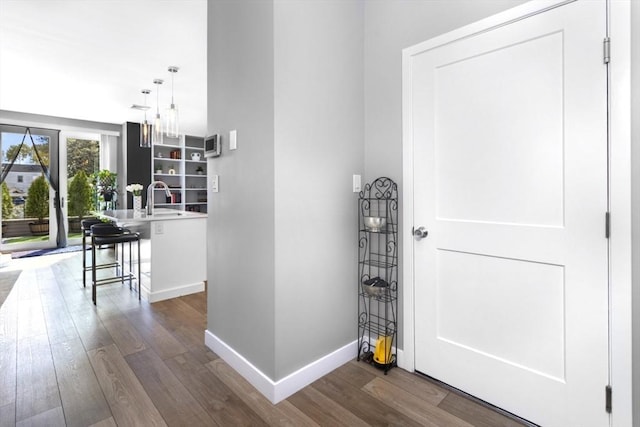 corridor featuring dark wood finished floors, baseboards, and a sink