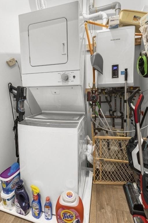 clothes washing area with stacked washing machine and dryer, wood finished floors, and water heater
