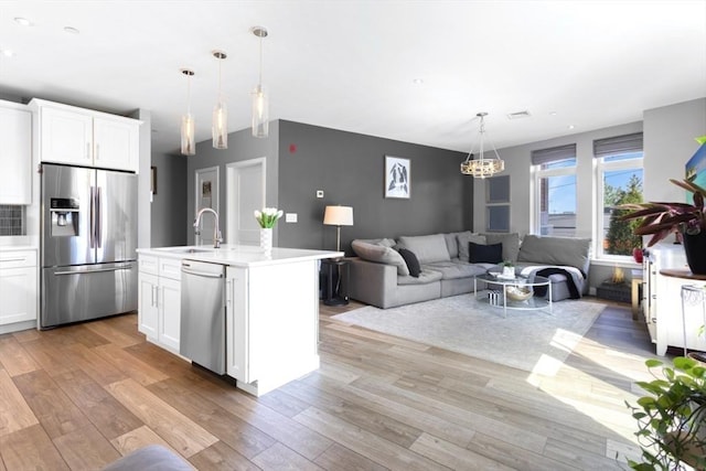 kitchen with appliances with stainless steel finishes, a sink, light countertops, light wood-style floors, and vaulted ceiling