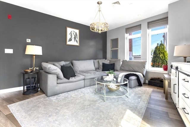 living room featuring an accent wall, wood finished floors, a chandelier, and baseboards