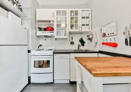 kitchen with tasteful backsplash, butcher block countertops, white appliances, white cabinetry, and a sink