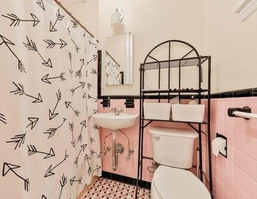 bathroom featuring a shower with curtain, tile walls, toilet, and a wainscoted wall