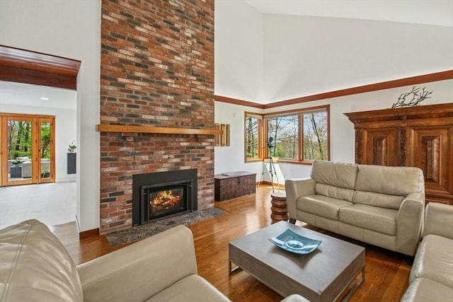 living area featuring a brick fireplace, a towering ceiling, wood finished floors, and baseboards