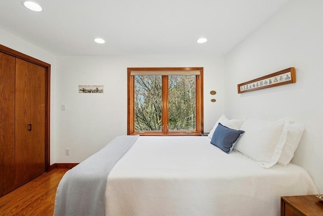bedroom with wood finished floors, a closet, recessed lighting, and baseboards
