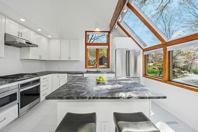 kitchen featuring light tile patterned floors, white cabinets, a sink, appliances with stainless steel finishes, and under cabinet range hood