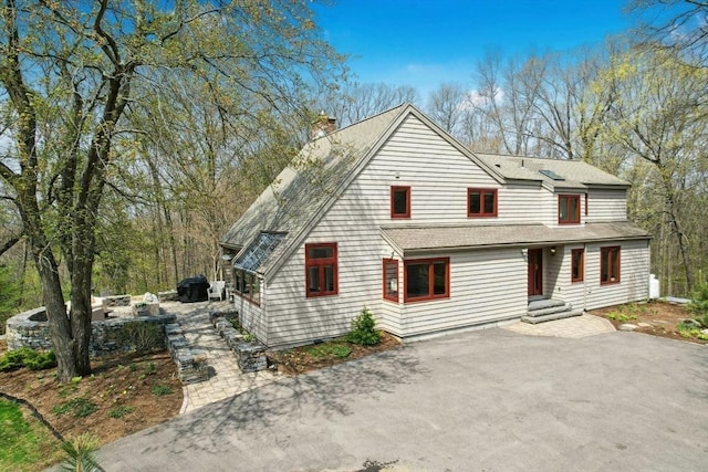 view of front of home with driveway, a shingled roof, and a chimney