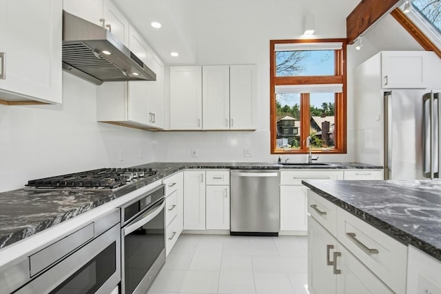 kitchen with a sink, under cabinet range hood, dark stone countertops, white cabinetry, and appliances with stainless steel finishes
