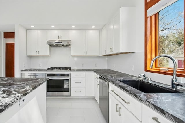 kitchen featuring under cabinet range hood, dark stone countertops, appliances with stainless steel finishes, and a sink