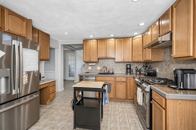 kitchen featuring appliances with stainless steel finishes, under cabinet range hood, a sink, tasteful backsplash, and recessed lighting
