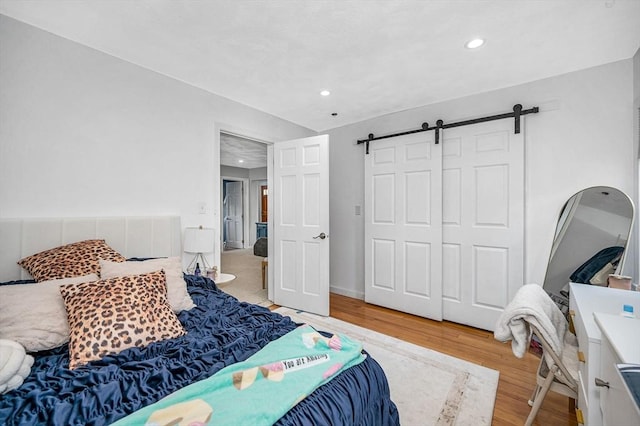 bedroom with wood finished floors, a barn door, recessed lighting, and a closet