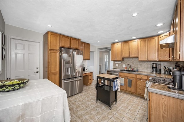 kitchen with stainless steel appliances, under cabinet range hood, a sink, backsplash, and recessed lighting