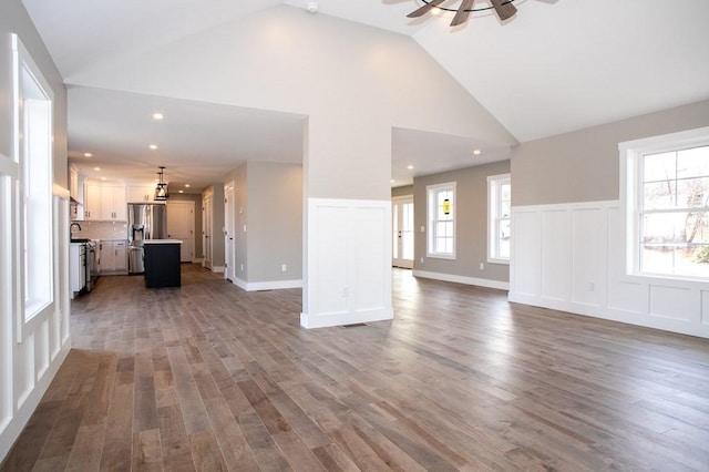 unfurnished living room with ceiling fan, plenty of natural light, high vaulted ceiling, and wood-type flooring