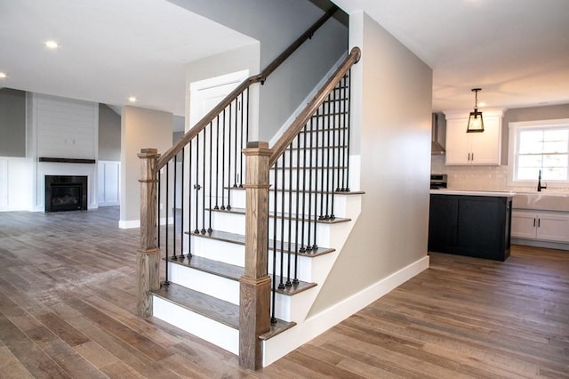 stairs featuring wood-type flooring, a fireplace, and sink