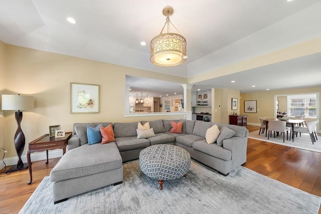 living area featuring ornate columns, wood finished floors, baseboards, and recessed lighting