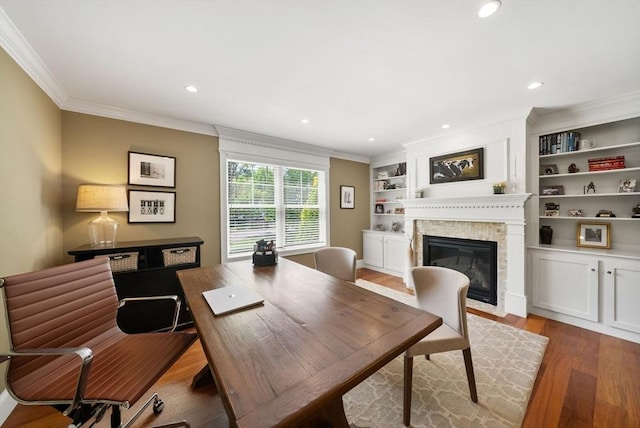 home office with wood finished floors, a fireplace with flush hearth, ornamental molding, recessed lighting, and built in features