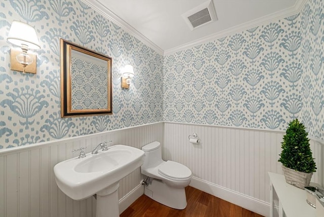 half bath with wood finished floors, wallpapered walls, toilet, wainscoting, and a sink