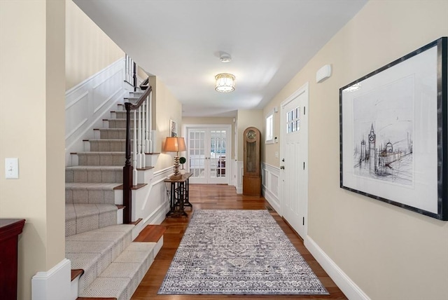 foyer entrance featuring stairs, dark wood finished floors, a decorative wall, a wainscoted wall, and french doors