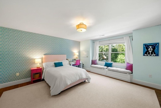 bedroom featuring wallpapered walls, baseboards, wood finished floors, and an accent wall