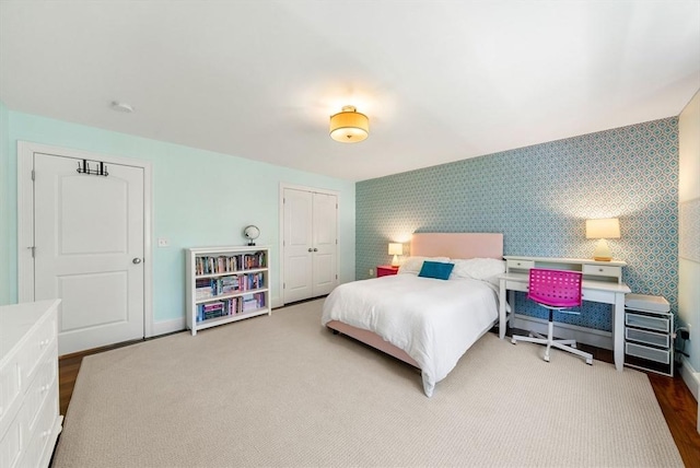 bedroom featuring wallpapered walls, a closet, baseboards, wood finished floors, and an accent wall