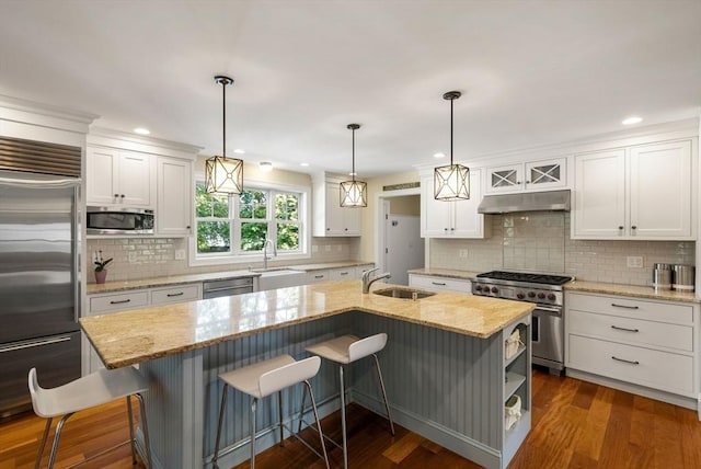 kitchen with built in appliances, under cabinet range hood, a sink, a center island with sink, and white cabinetry