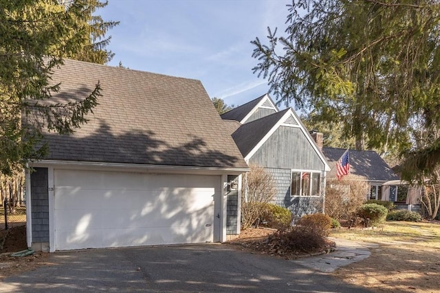 exterior space with a detached garage, roof with shingles, and a chimney