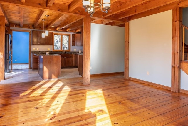 kitchen with dark countertops, a kitchen island, beamed ceiling, light wood-type flooring, and freestanding refrigerator