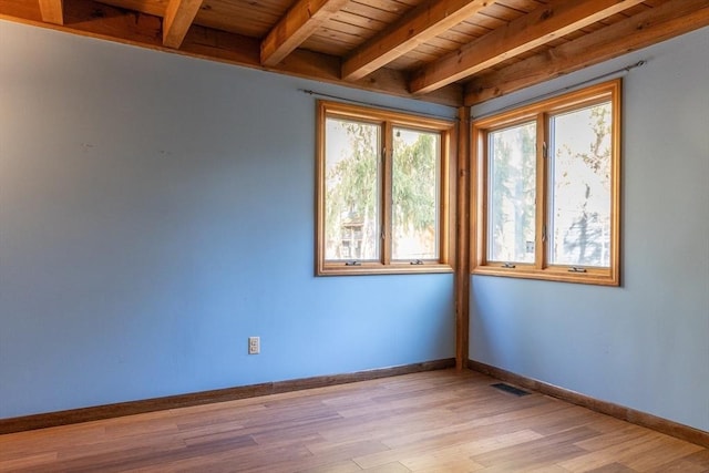 empty room featuring light wood-style floors, beamed ceiling, visible vents, and baseboards