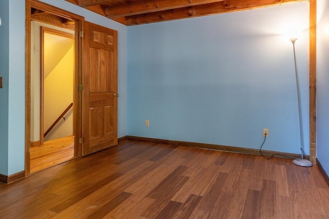 unfurnished room featuring beam ceiling, wood finished floors, and baseboards