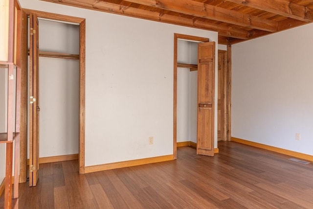 unfurnished bedroom with visible vents, beam ceiling, baseboards, and wood finished floors