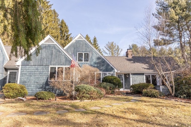 view of front of property with a shingled roof, a front yard, and a chimney