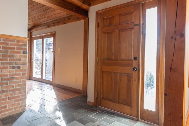 foyer with stone tile floors, vaulted ceiling with beams, wood ceiling, and baseboards