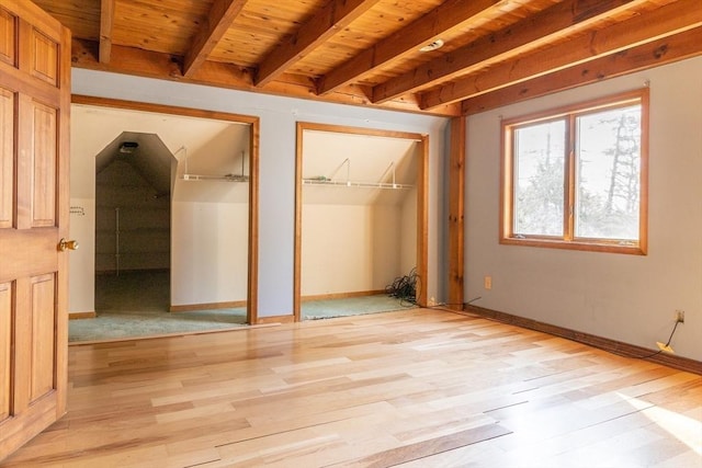 unfurnished bedroom featuring baseboards, multiple closets, beamed ceiling, wooden ceiling, and light wood-style floors