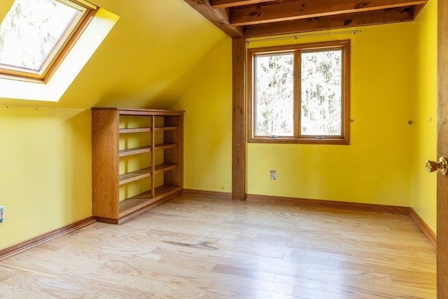 bonus room with light wood finished floors, vaulted ceiling with skylight, and baseboards