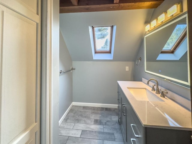 bathroom with vaulted ceiling with skylight, vanity, and baseboards