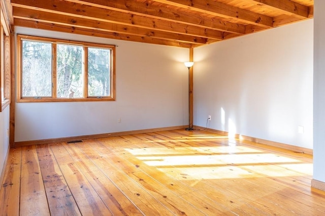 unfurnished room featuring beamed ceiling, visible vents, baseboards, and wood-type flooring