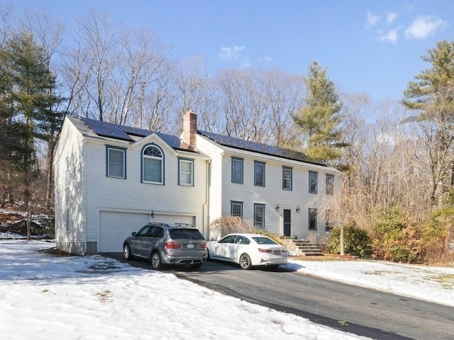 colonial inspired home featuring driveway, an attached garage, a chimney, and solar panels