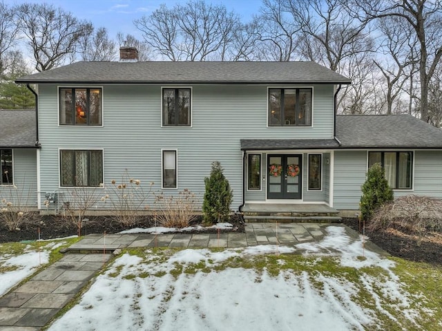 view of front of property with french doors, a chimney, and a shingled roof