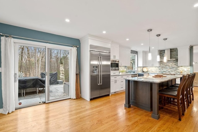 kitchen with backsplash, white cabinets, wall chimney range hood, and built in appliances