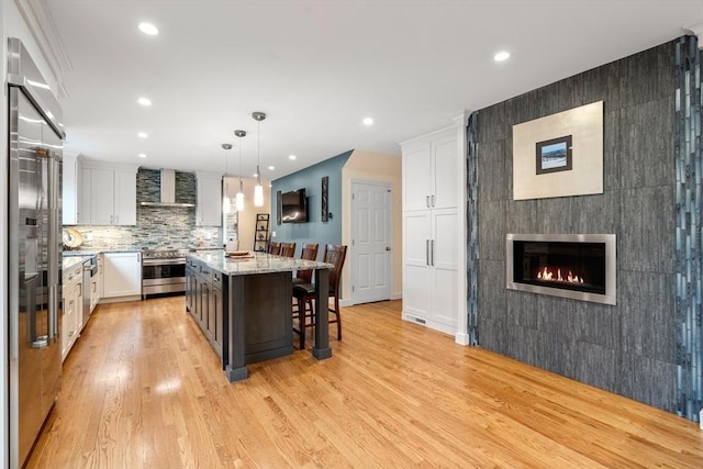 kitchen featuring light wood-type flooring, wall chimney exhaust hood, white cabinets, and a kitchen breakfast bar