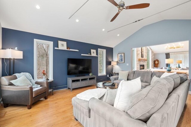 living room with recessed lighting, ceiling fan with notable chandelier, a fireplace, light wood-style floors, and vaulted ceiling