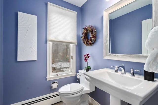 half bathroom featuring baseboard heating, a sink, and toilet