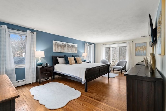 bedroom with a baseboard radiator, multiple windows, and hardwood / wood-style floors