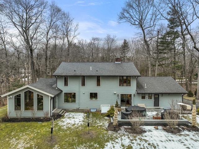 snow covered back of property with roof with shingles, a lawn, and a chimney