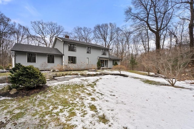 snow covered rear of property with a chimney