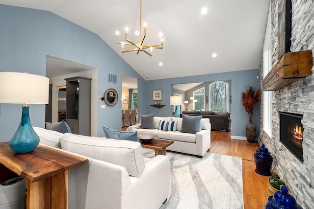 living area featuring visible vents, a chandelier, a stone fireplace, light wood-type flooring, and high vaulted ceiling