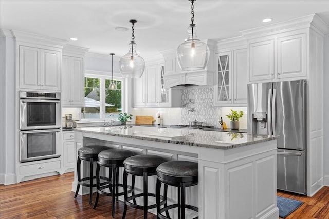 kitchen with a kitchen island, pendant lighting, white cabinetry, stainless steel appliances, and light stone countertops