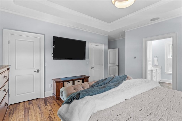 bedroom with hardwood / wood-style flooring, ornamental molding, ensuite bathroom, and a raised ceiling