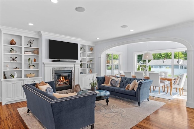 living room with built in shelves, ornamental molding, and light hardwood / wood-style floors