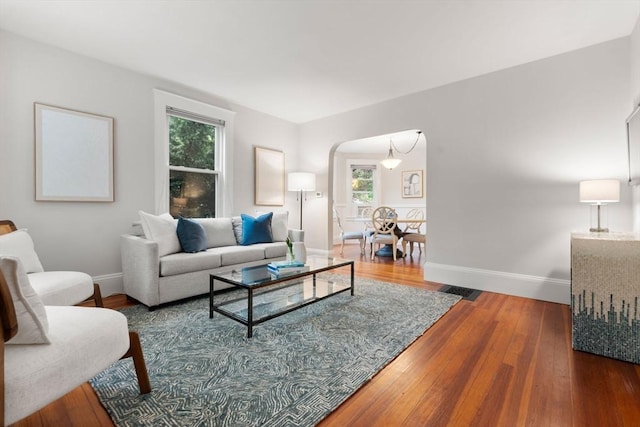 living area with arched walkways, wood finished floors, and baseboards